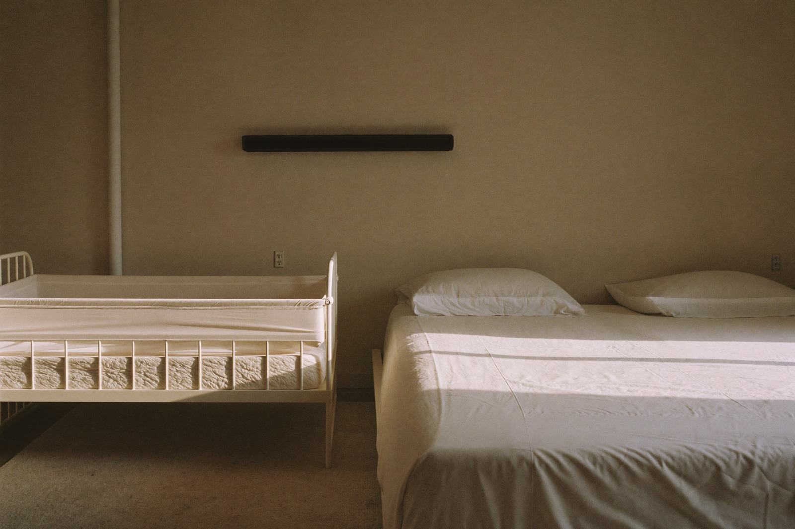 Cuna de madera junto a una cama de matrimonio en una recámara con luz suave de la tarde