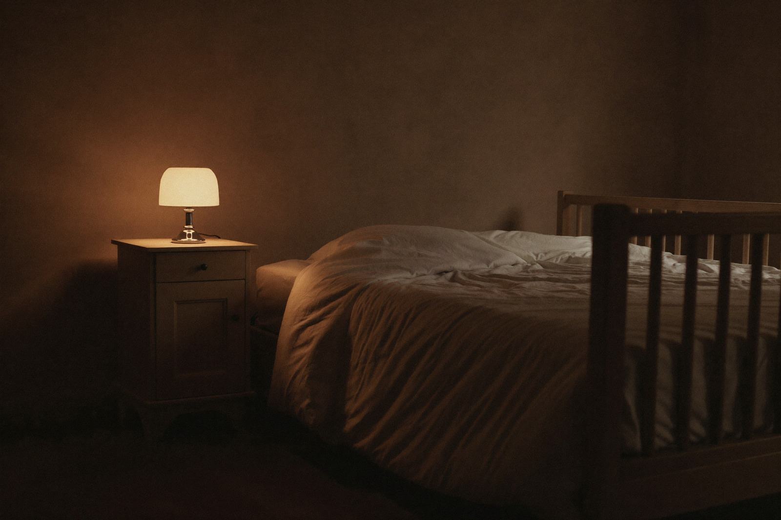 Recámara en penumbra con una lámpara de mesa encendida a baja intensidad junto a una cuna