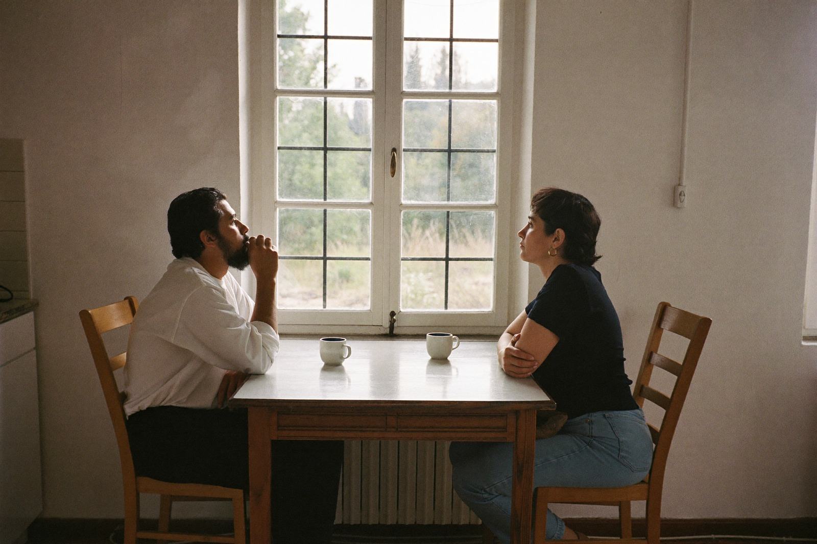 Dos adultos sentados a la mesa de la cocina, conversando con un café, con la luz de la mañana en la ventana