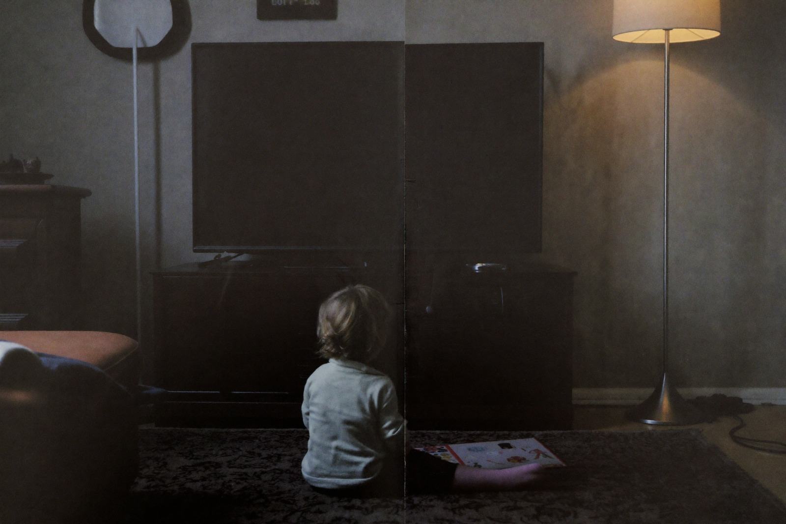 Sala de noche con la televisión apagada y un niño sentado en el tapete mirando un libro bajo la lámpara