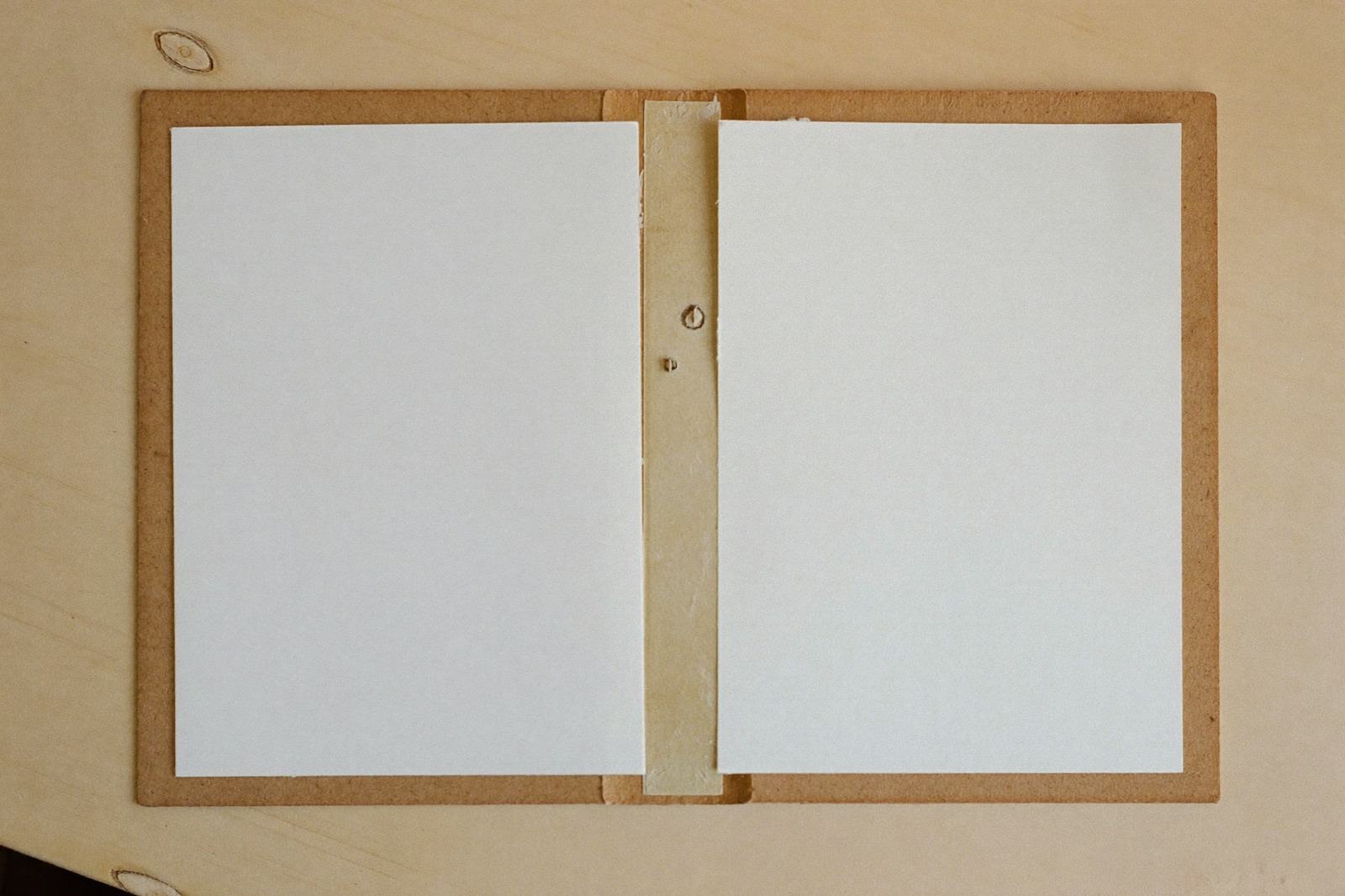 Carpeta de archivo lisa abierta con hojas en blanco, sobre una superficie de madera clara