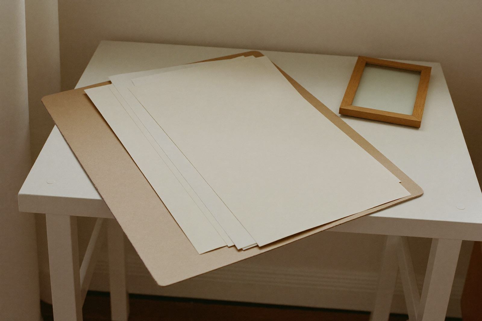 Carpeta lisa con documentos dentro sobre una mesa clara, junto a un portarretratos pequeño sin imagen