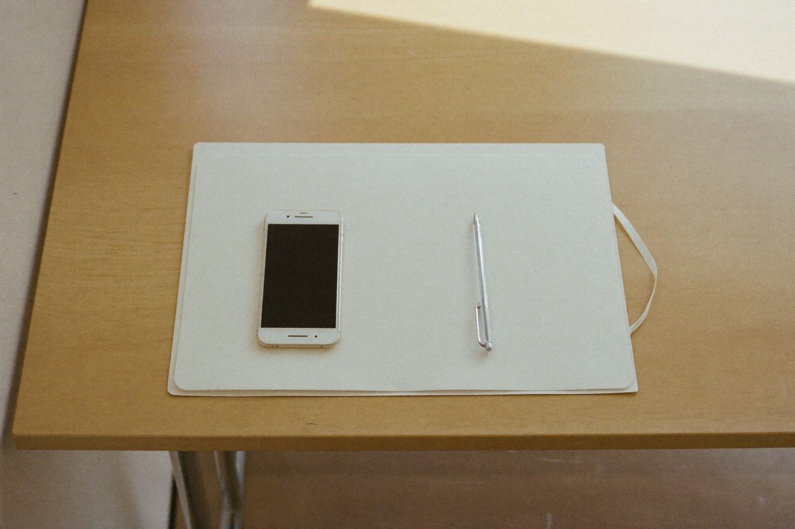Mesa de madera clara con una carpeta cerrada, un bolígrafo y un teléfono encima