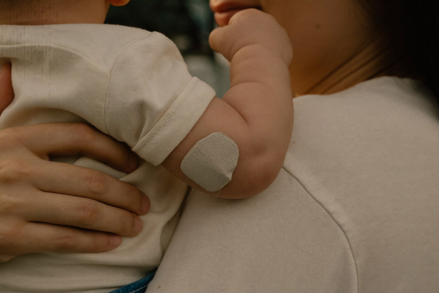 Una curita clara pegada en el brazo de un bebé que su mamá carga contra el hombro, después de la vacuna