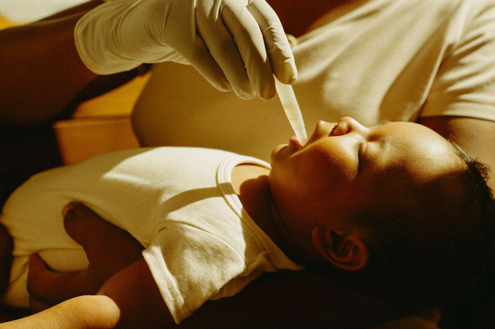 Manos de personal de salud dando una vacuna en gotas a un bebé sostenido por su madre