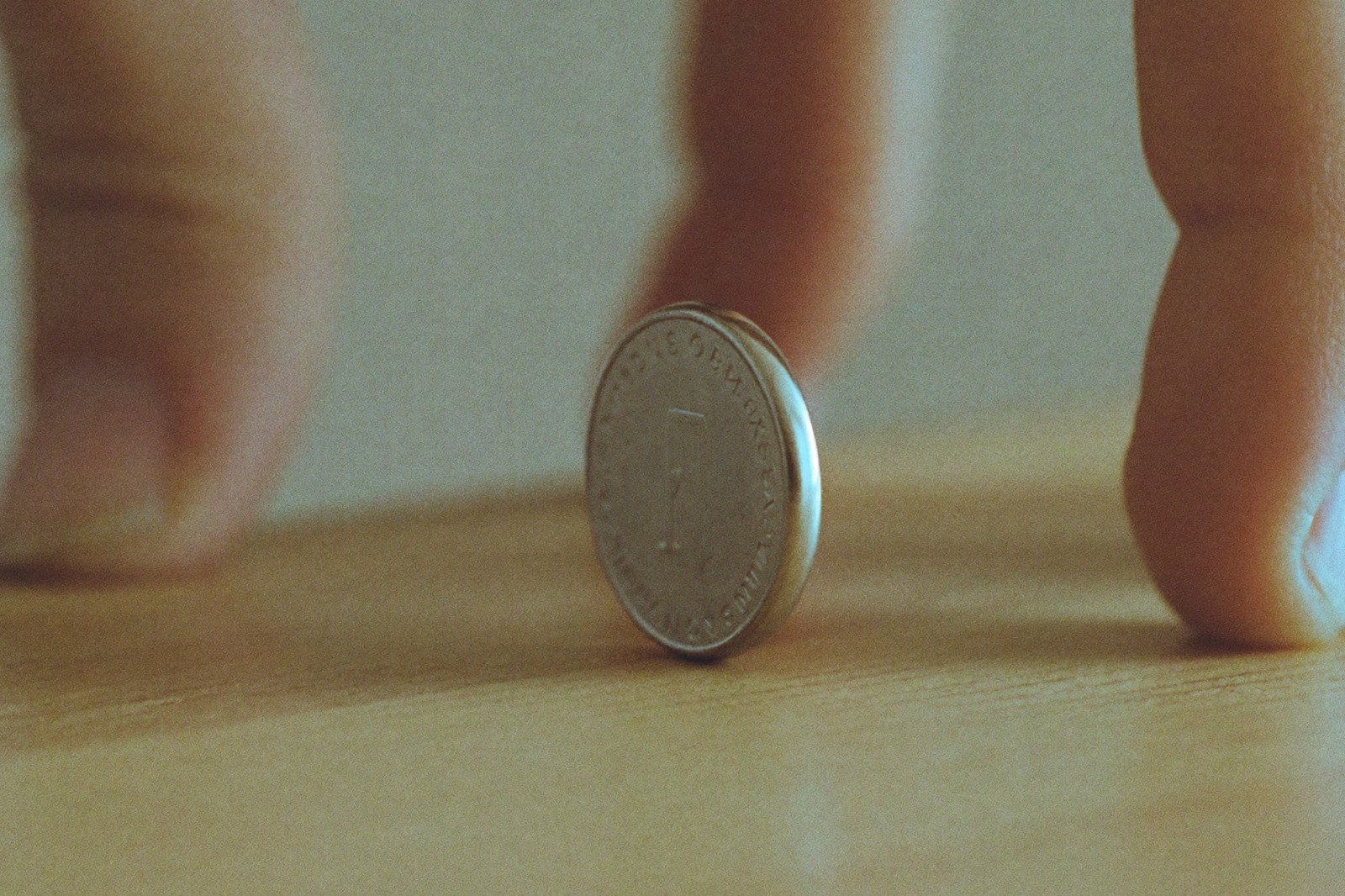 Primer plano de una pila botón de canto sobre una mesa de madera, entre las yemas de dos dedos