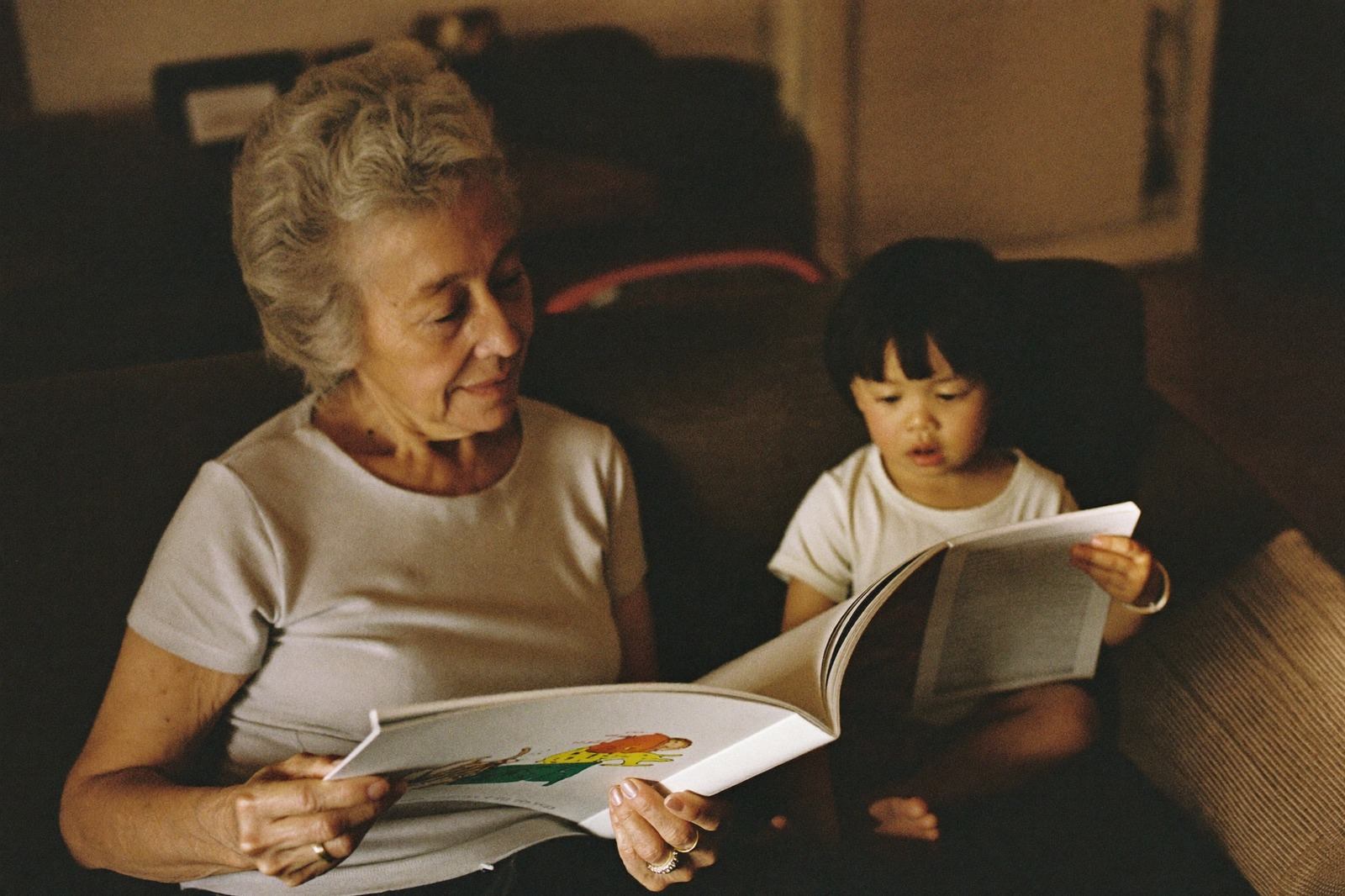Persona mayor leyendo un libro ilustrado junto a un niño pequeño sentado a su lado