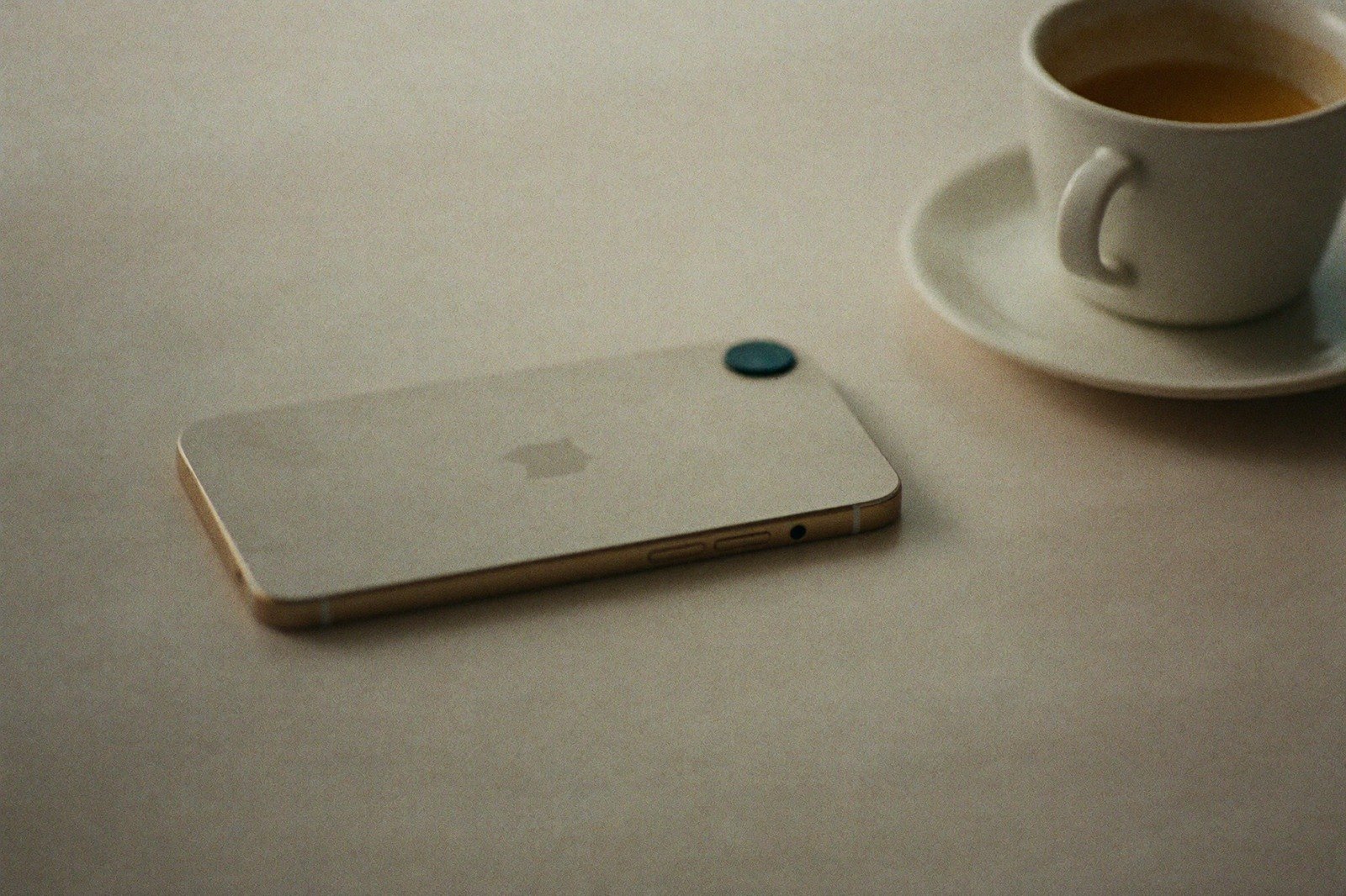 Teléfono celular apoyado boca abajo sobre una mesa de madera junto a una taza