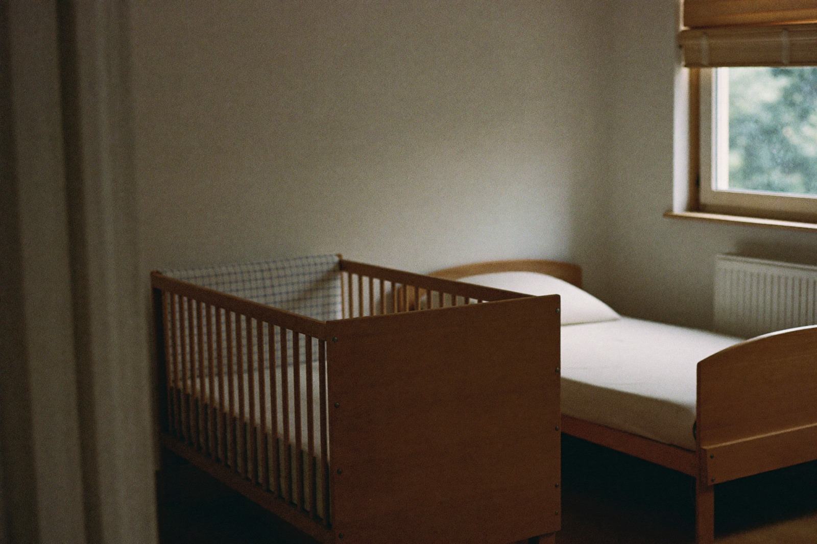 Cuarto infantil con una cuna y una cama pequeña junto a una ventana