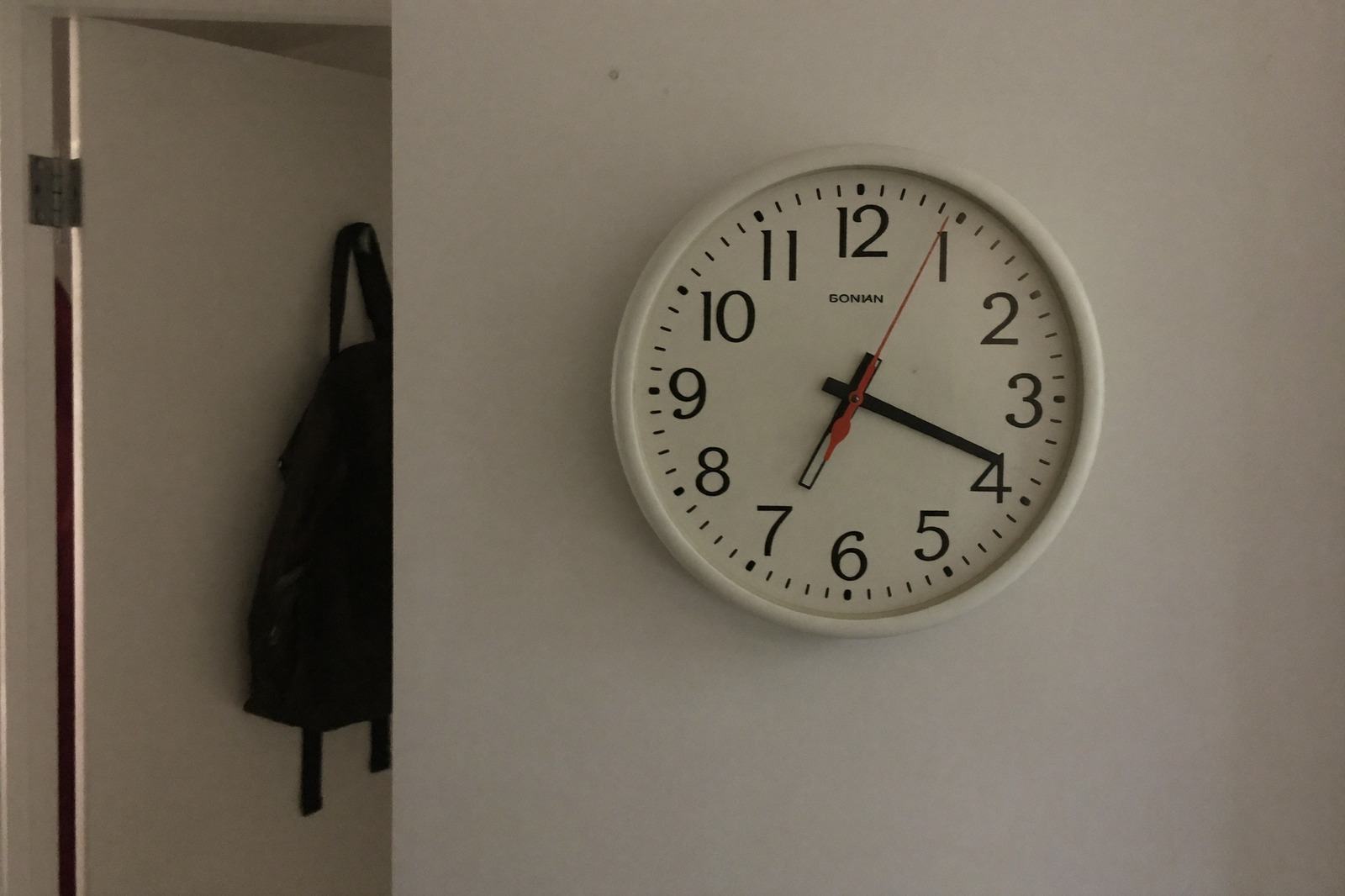 Reloj de pared sencillo en una pared clara junto a una repisa con juguetes