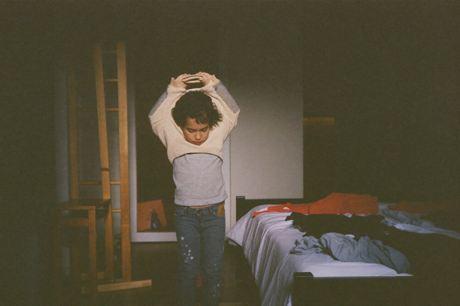 Niño pequeño poniéndose la camiseta él solo junto a su cama