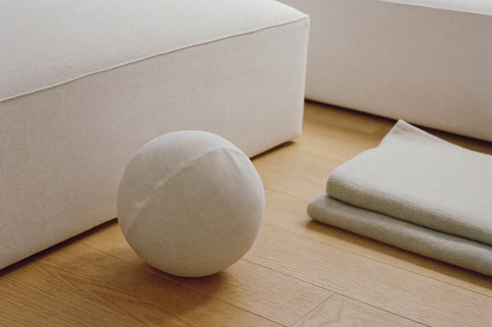 Pelota blanda de tela sobre el piso de madera, junto a una manta doblada en una sala luminosa