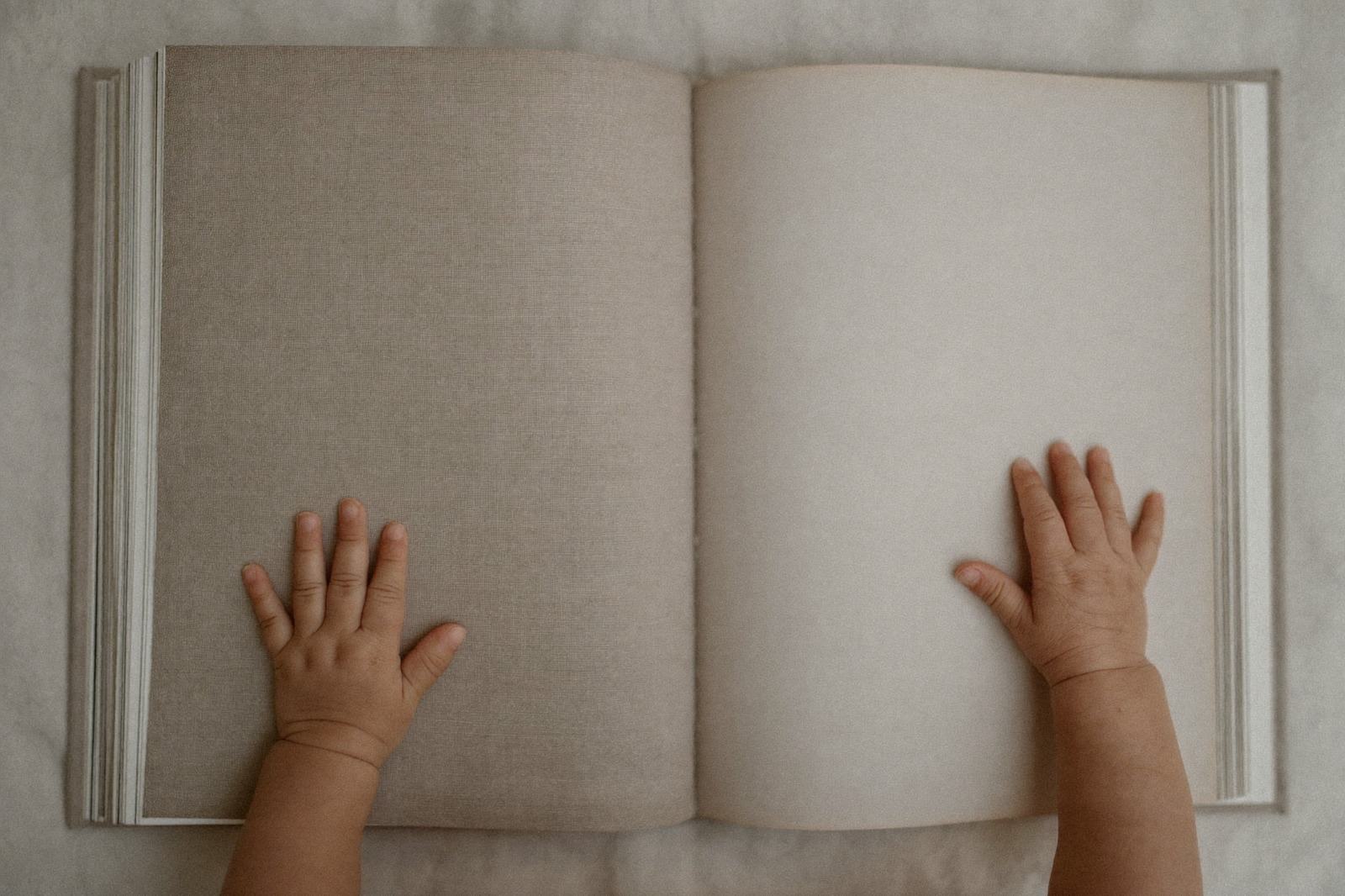 Libro de tela abierto sobre una manta clara, con las manos de un bebé sobre la página
